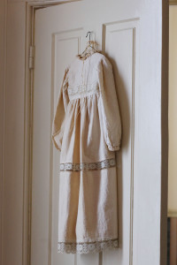 A child's antique dress hanging from the back of a door.
