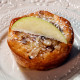 A muffin on a white plate with almonds and a slice of apple on the top