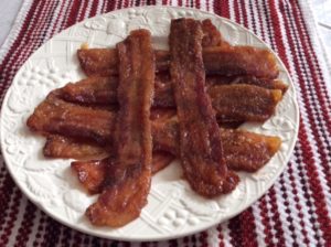 Slices of candied bacon on a white plate and a red and white place mat