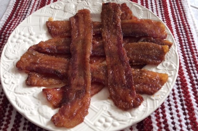 Slices of candied bacon on a white plate and a red and white place mat